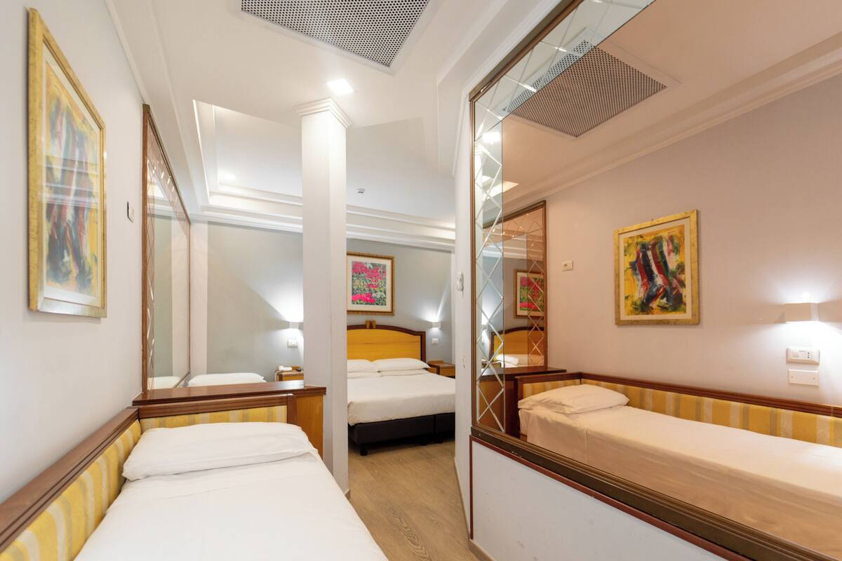 A hotel room with a bed, a mirror, a bedside table, and a wall with a painting.