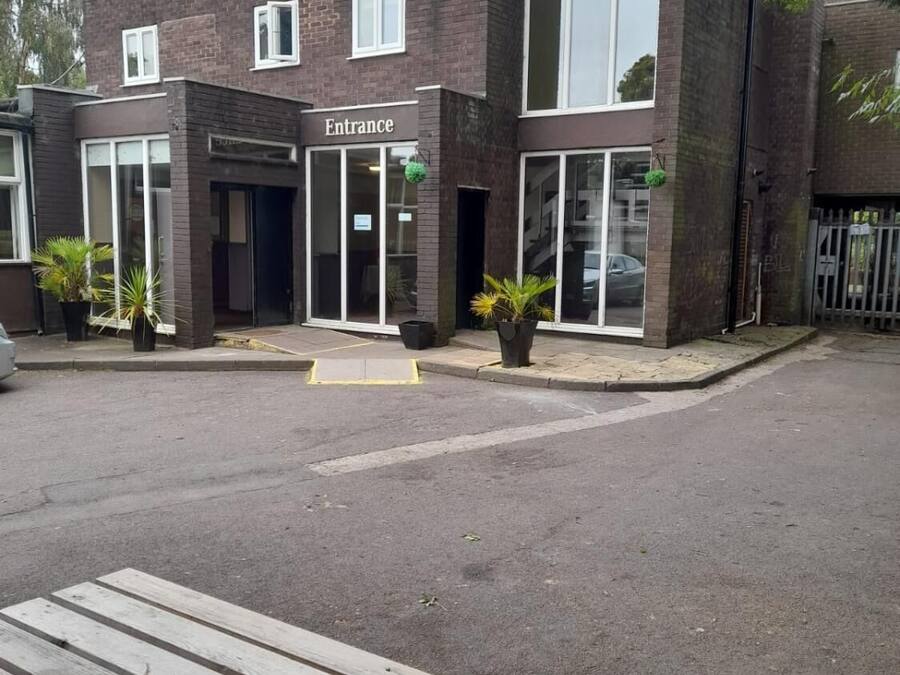 A building with an 'Entrance' sign, large windows, and potted plants.