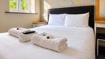 A hotel room with a bed, a nightstand, a window, and a wall with a leaf pattern.
