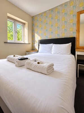 A hotel room with a bed, a nightstand, a window, and a wall with a leaf pattern. - The Avenue Lodge (Birmingham)