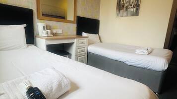 A hotel room with two beds, a desk with a mirror, a remote control, and a wall with a patterned wallpaper.