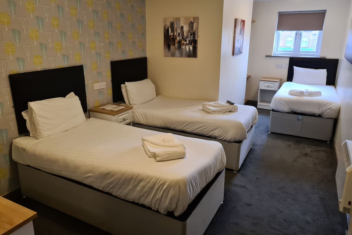 Una camera d'albergo con due letti singoli, un piccolo comodino con lampada, un quadro appeso al muro e una finestra con persiane.