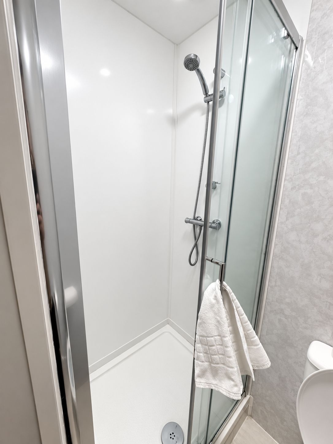 A glass-enclosed shower with a handheld showerhead and a towel hanging on the door.