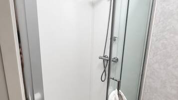 A glass-enclosed shower with a handheld showerhead and a towel hanging on the door.