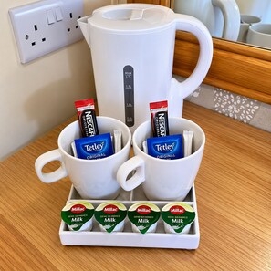 A kitchen counter with a coffee maker, two cups with coffee pods, and a tray of milk cartons. - The Avenue Lodge (Birmingham)