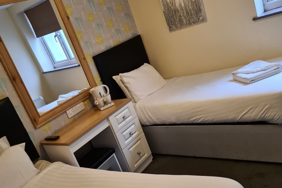Una camera d'albergo con due letti, una scrivania con una sedia, uno specchio, una finestra e un quadro appeso al muro.