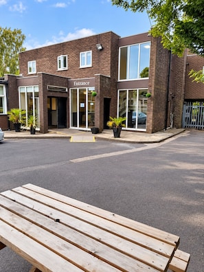 A building with a sign labeled 'Entrance' and a paved area with a wooden bench in the foreground. - The Avenue Lodge (Birmingham)