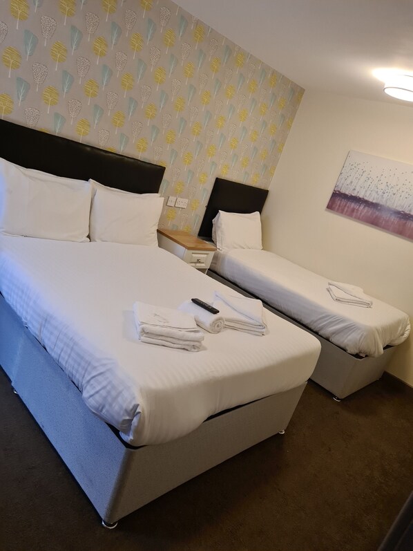 A hotel room with two beds, a nightstand, and a painting on the wall. - The Avenue Lodge (Birmingham)