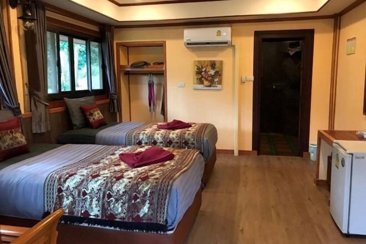 Une chambre avec deux lits, une armoire, un climatiseur et une petite kitchenette.