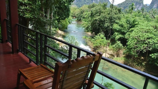 A wooden chair on a balcony overlooking a river surrounded by lush greenery and mountains. - Khaosok Rainforest Resort (Phanom)