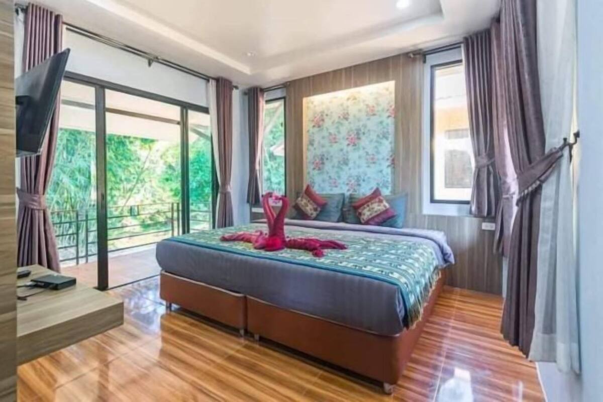 Une chambre avec un grand lit, une télévision, un plancher en bois et une vue sur la verdure.