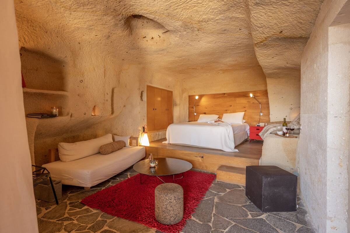 A cozy, cave-like bedroom with a bed, sofa, and a small table.