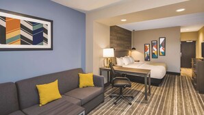 Habitación de hotel con un sofá gris, una mesita, un escritorio con una silla, una cama y una alfombra a rayas.
