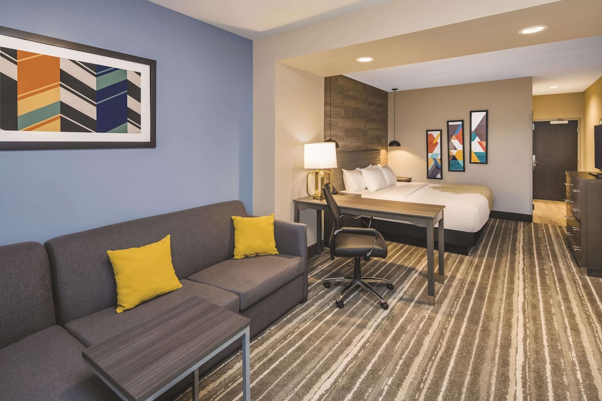 Une chambre d’hôtel avec un canapé gris, une petite table, un bureau avec une chaise, un lit et un tapis à rayures.