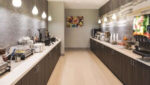 Una cocina moderna con una encimera larga, iluminación en el techo y un dispensador de zumo de frutas.
