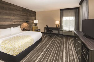 A hotel room with a large bed, a desk with a chair, a TV, and a window with curtains.