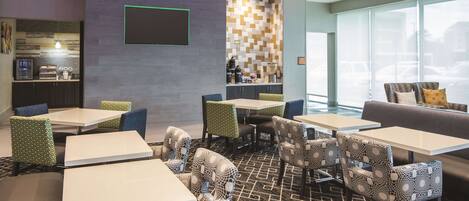 A modern hotel lobby with multiple seating areas, a bar, and a visible kitchen area.