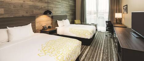 A hotel room with two beds, a desk, a chair, a TV, and a large window with curtains.