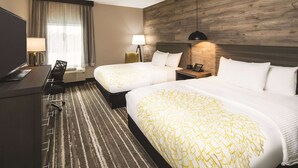 Une chambre d’hôtel avec deux lits, un bureau, une chaise, une lampe et un téléviseur.
