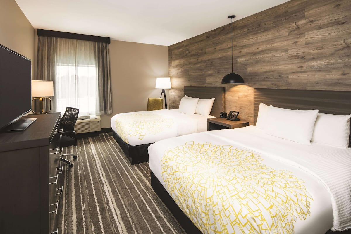 Une chambre d’hôtel avec deux lits, un bureau, une chaise, une lampe et un téléviseur.