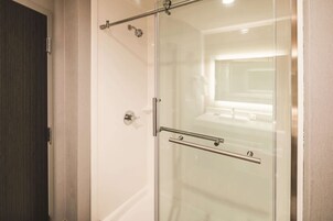 Un baño moderno con cabina de ducha de vidrio, una puerta de madera oscura y un revestimiento de pared blanco.