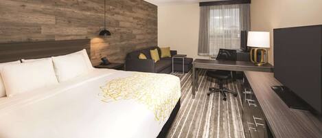 Una habitación de hotel con una cama grande, un escritorio, una silla, una lámpara y un televisor.
