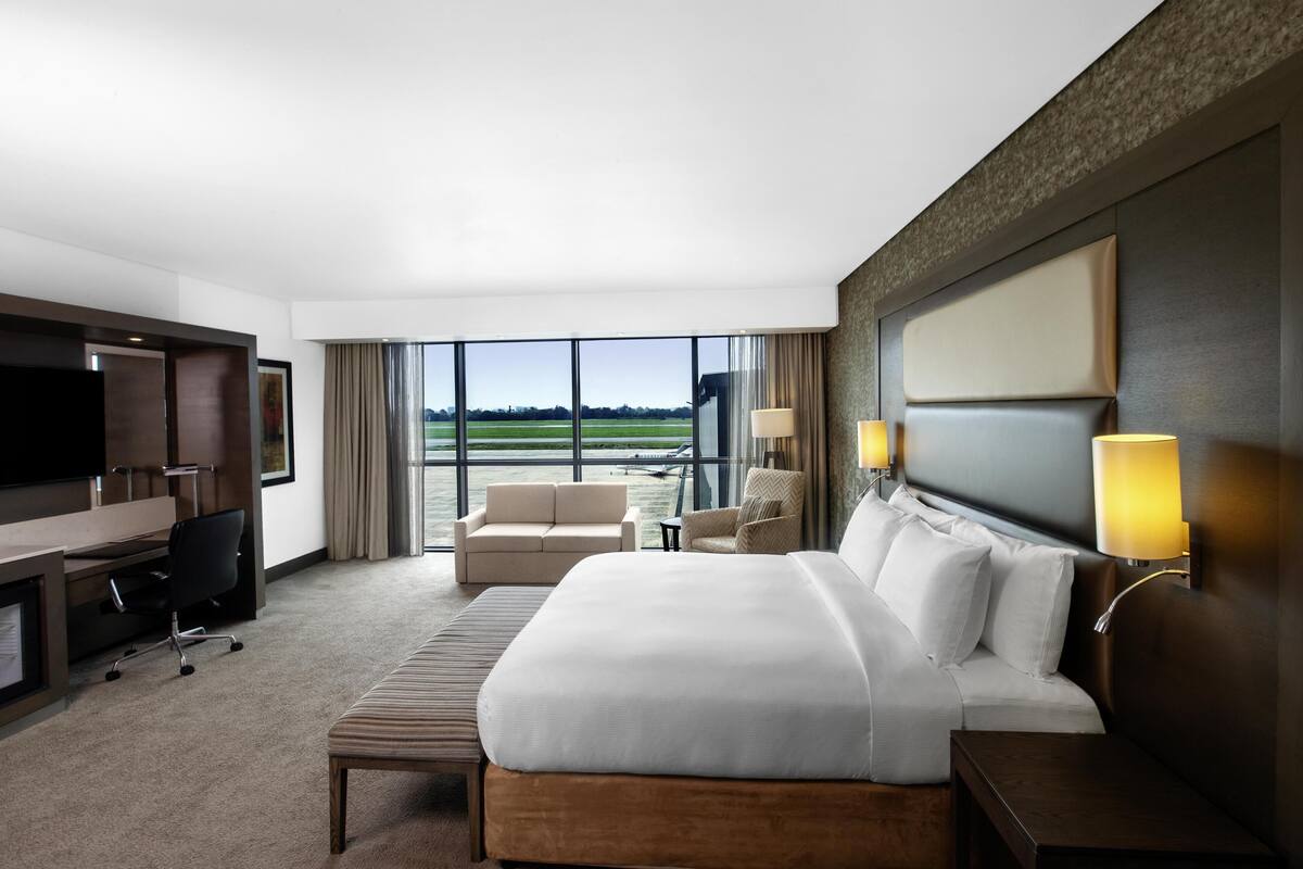 Habitación de hotel con cama, escritorio, silla y un amplio ventanal con vistas al exterior.