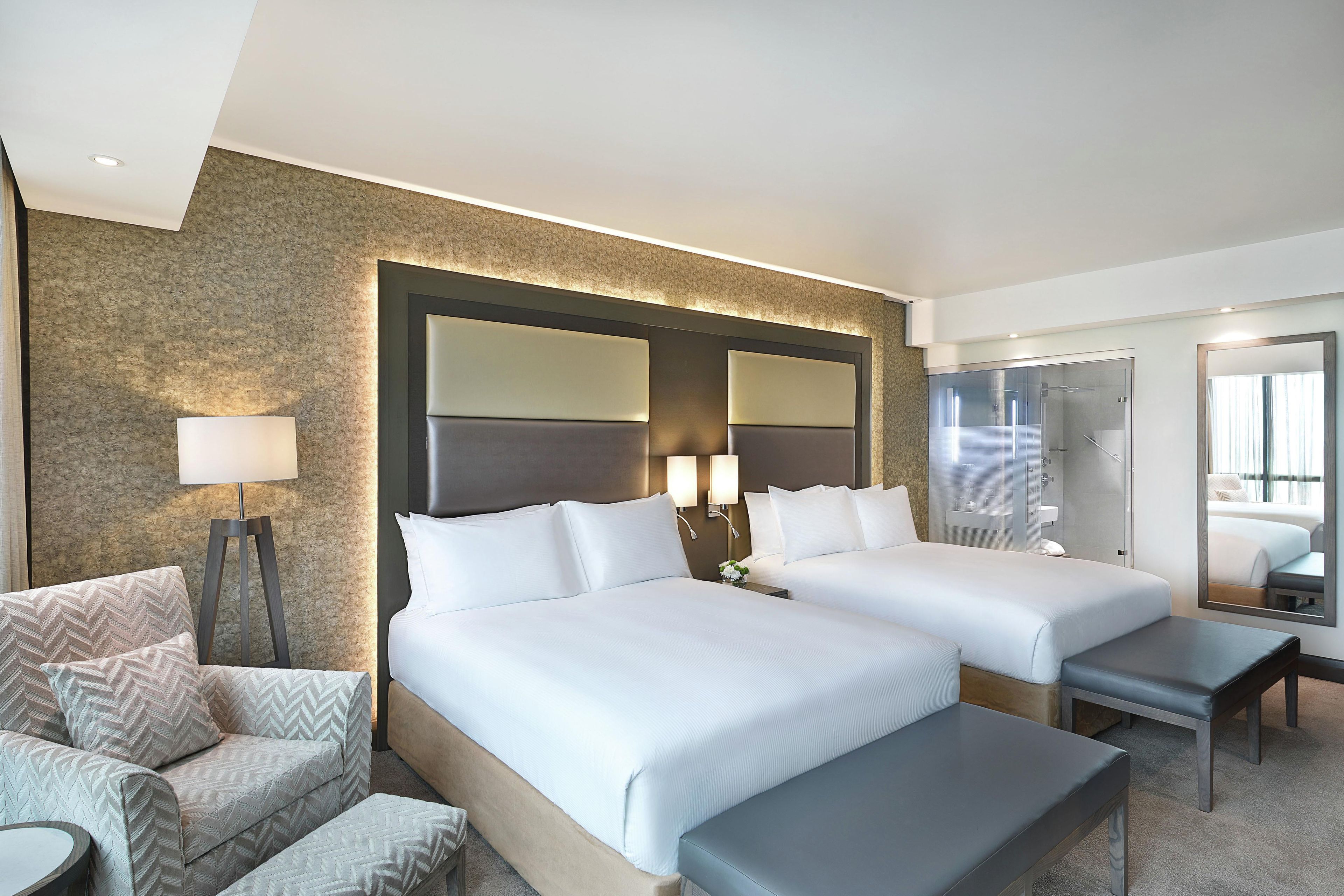 A hotel room with two beds, a sofa, a desk, a mirror, and a lamp.