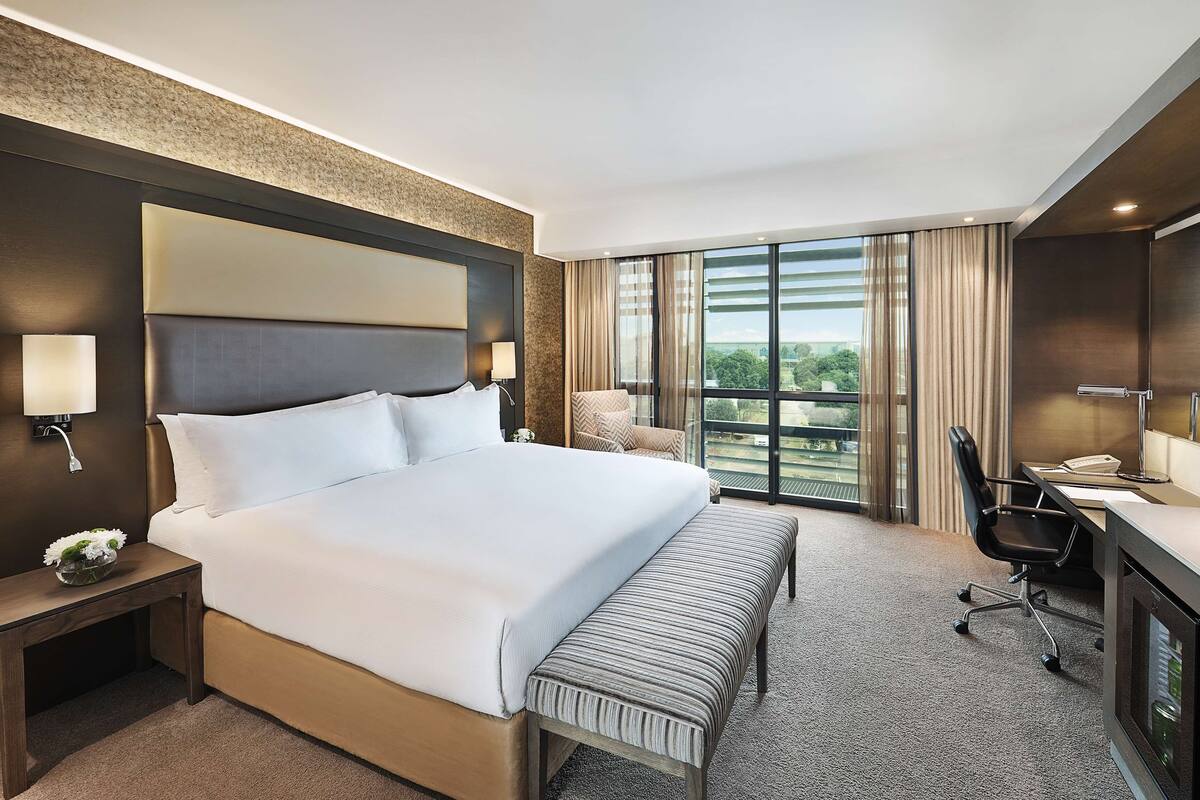 Habitación de hotel con una cama grande, un escritorio con silla, televisor y vistas al exterior.