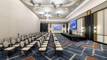 A conference room with rows of chairs, a stage, and a large screen.