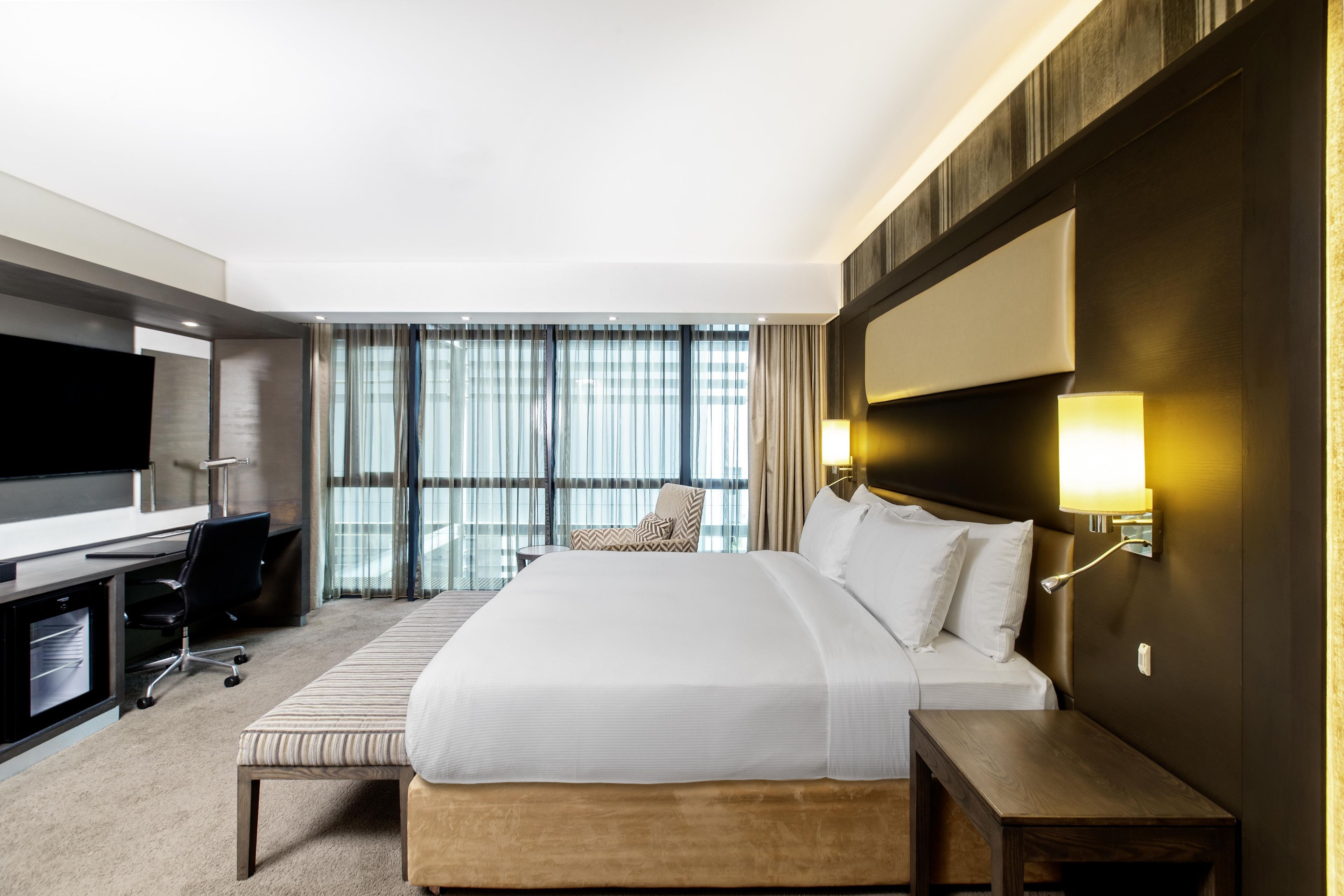 A hotel room with a large bed, a desk, a chair, a TV, and a window with curtains.