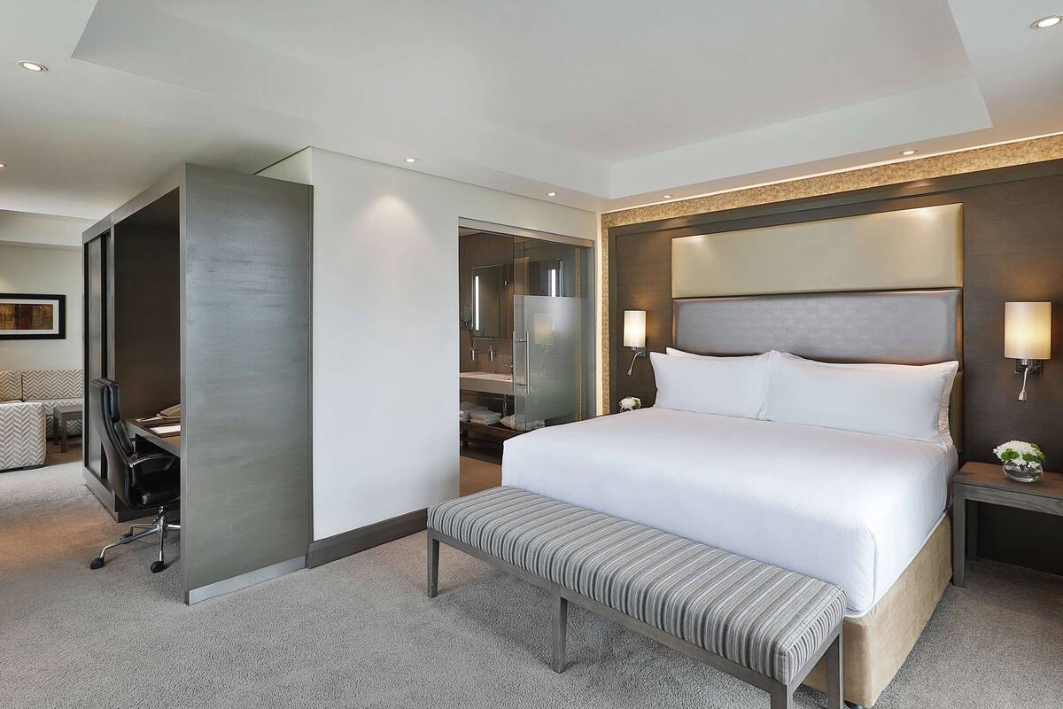 Una habitación de hotel moderna con una cama grande, un banco, un escritorio y un vestidor.