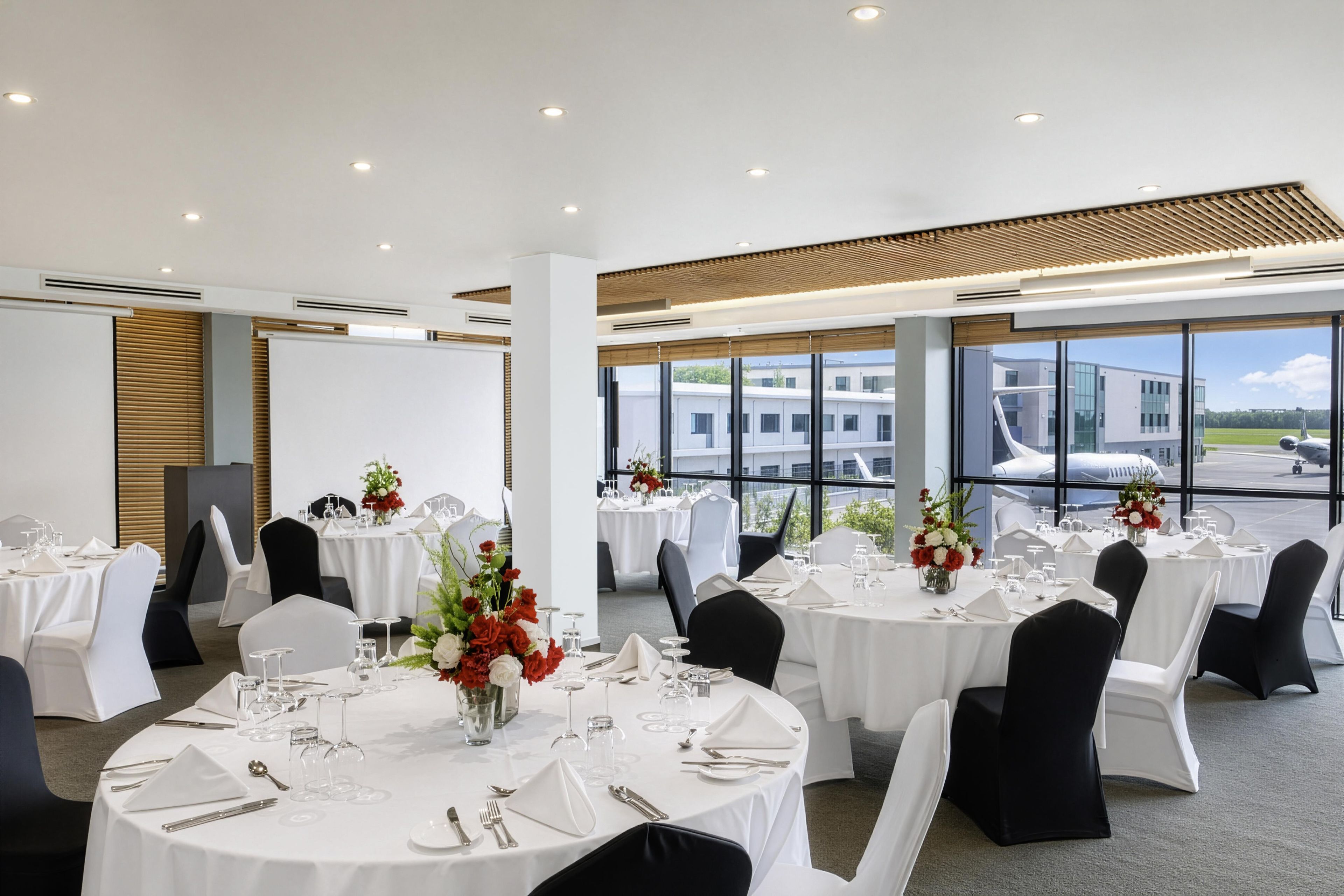 Une salle de conférence avec des tables rondes, des nappes blanches, des chaises noires et des centres de table floraux.