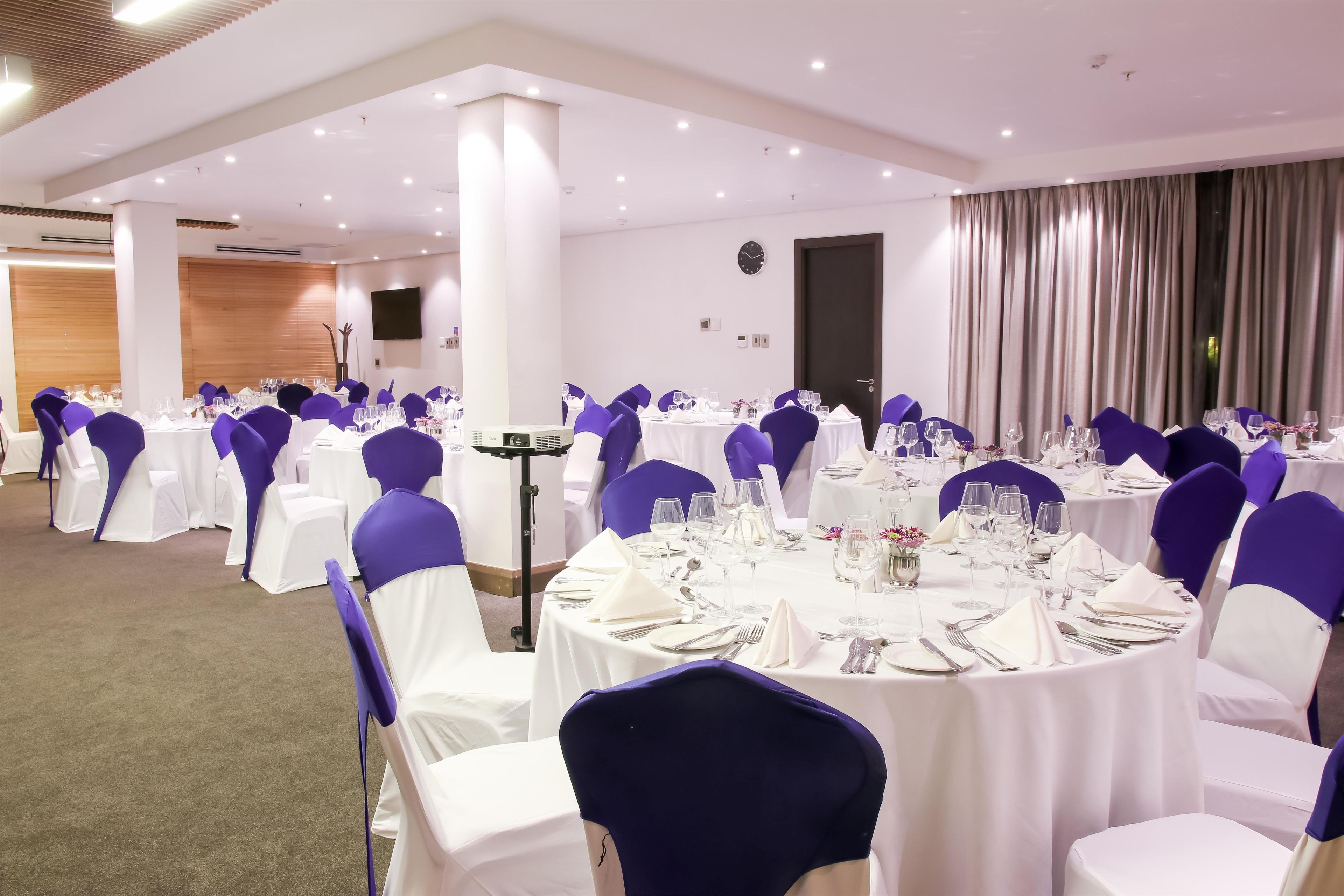 A banquet hall with round tables, white tablecloths, and purple chair covers.