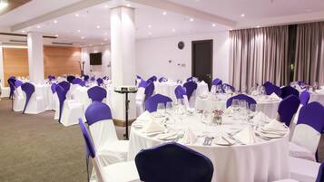 A banquet hall with round tables, white tablecloths, and purple chair covers.