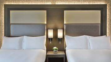 A hotel room with two beds, a nightstand, and wall-mounted lamps.