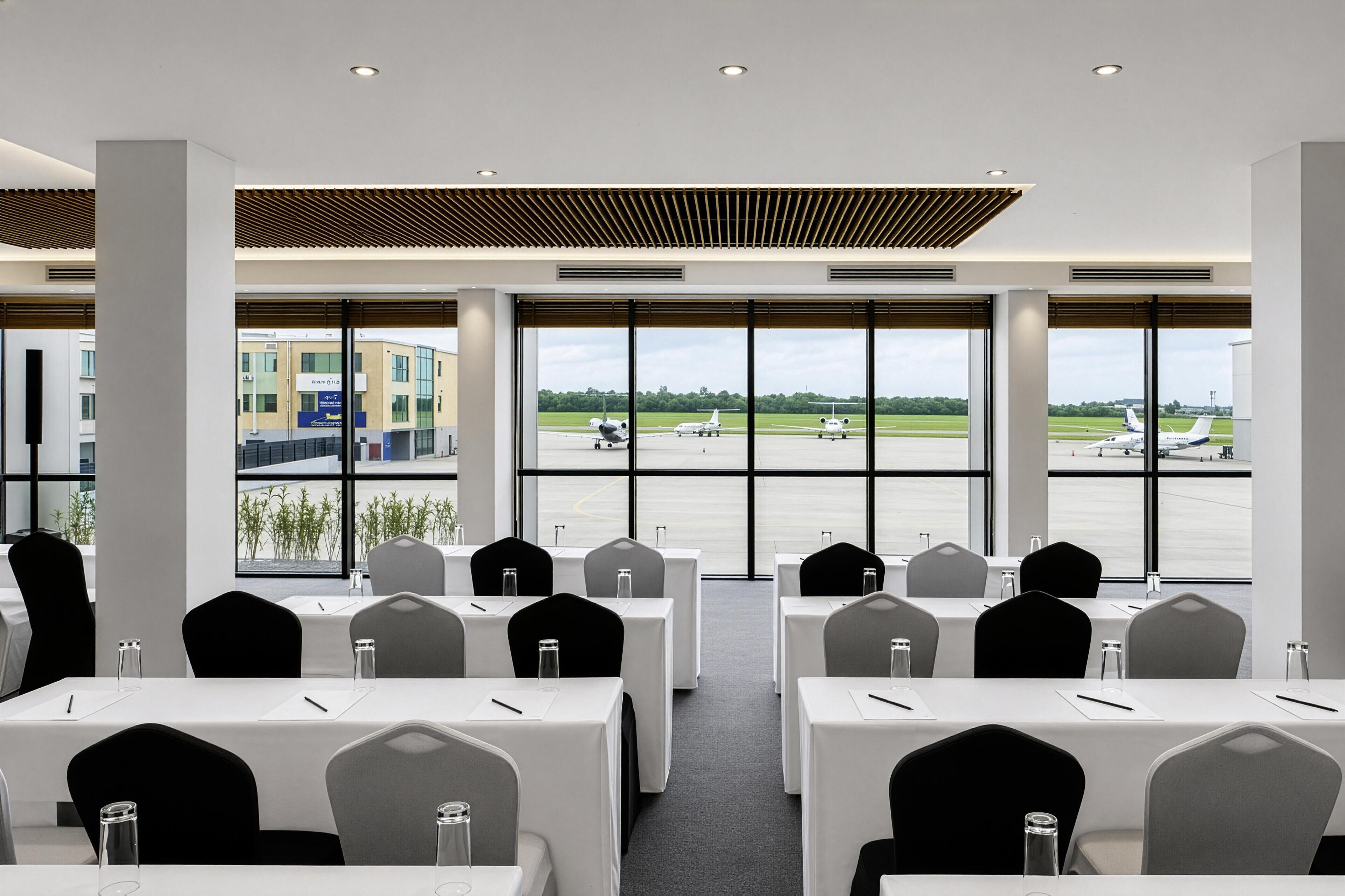Une salle de conférence équipée de tables et de chaises, avec de grandes fenêtres donnant sur un aéroport.