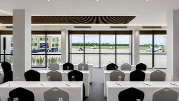Une salle de conférence équipée de tables et de chaises, avec de grandes fenêtres donnant sur un aéroport.