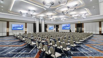 Un salón de conferencias con filas de sillas, pantallas grandes e iluminación de techo moderna.