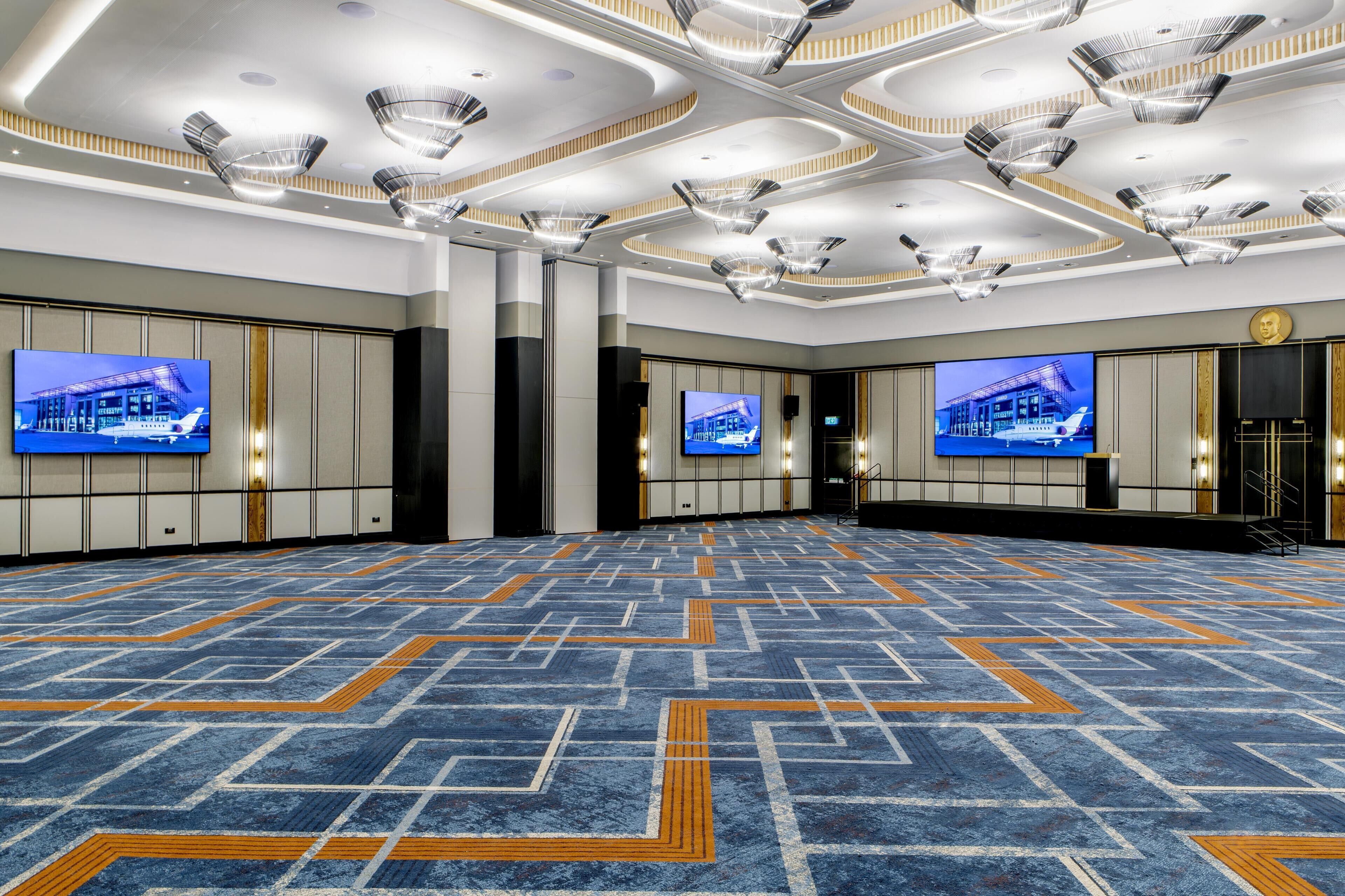 A spacious conference room with a patterned carpet, multiple screens, and a modern ceiling design.