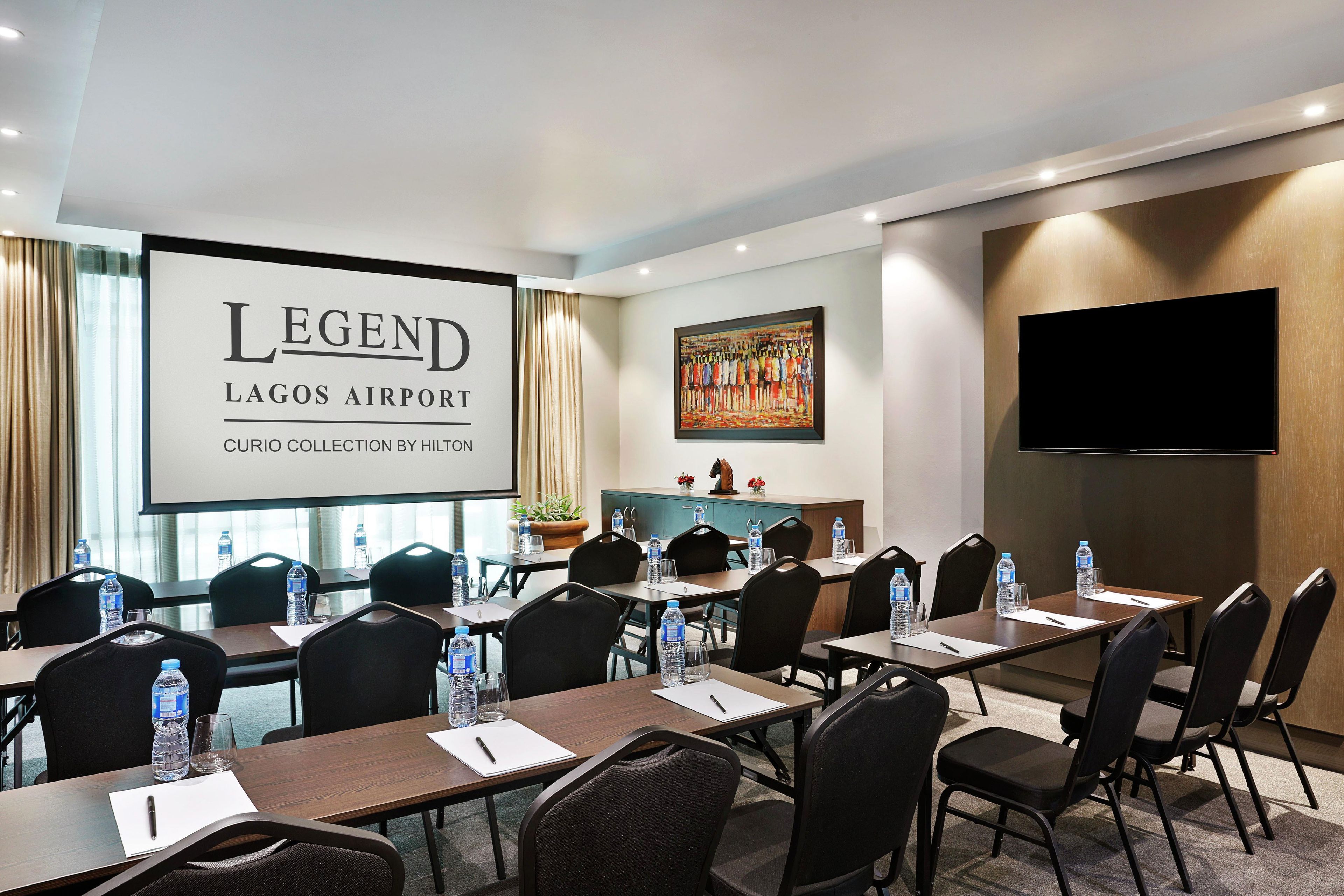 Une salle de conférence dotée d’un grand écran affichant la mention : « LEGEND LAGOS AIRPORT CURIO COLLECTION BY HILTON ».