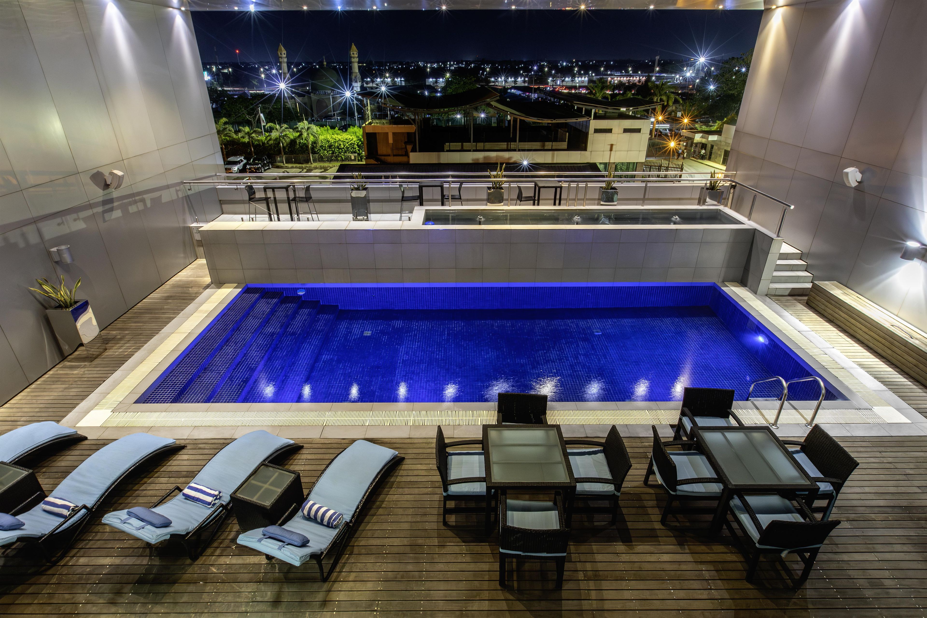 A rooftop pool with lounge chairs and a table, surrounded by a wooden deck.