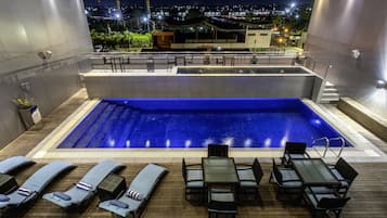 A rooftop pool with lounge chairs and a table, surrounded by a wooden deck.