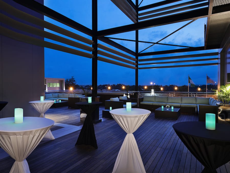 A rooftop terrace with tables and chairs, a view of the city skyline, and a flag.