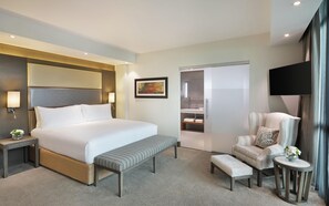 A hotel room with a large bed, a bench, a chair, a small table with a vase, a painting on the wall, and a television. - Legend Hotel Lagos Airport, Curio Collection by Hilton (Lagos)