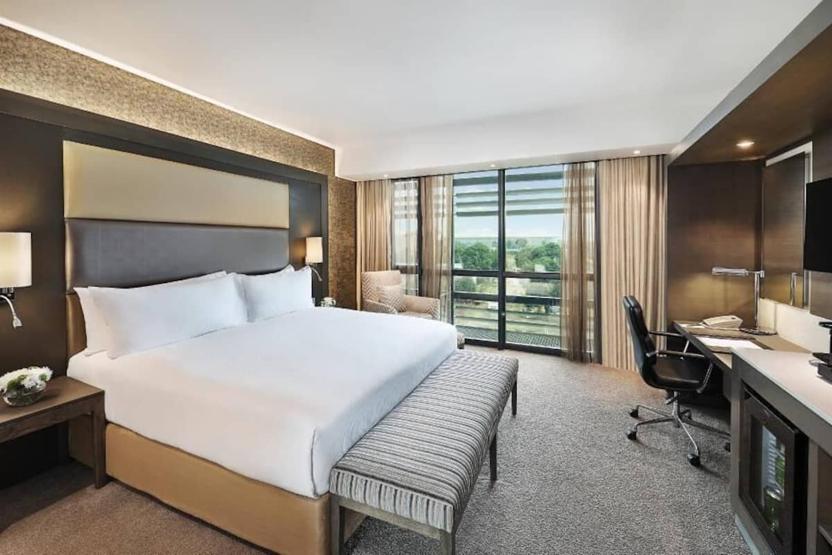 Una habitación de hotel con una cama grande, un escritorio con silla, un televisor y una ventana con cortinas.