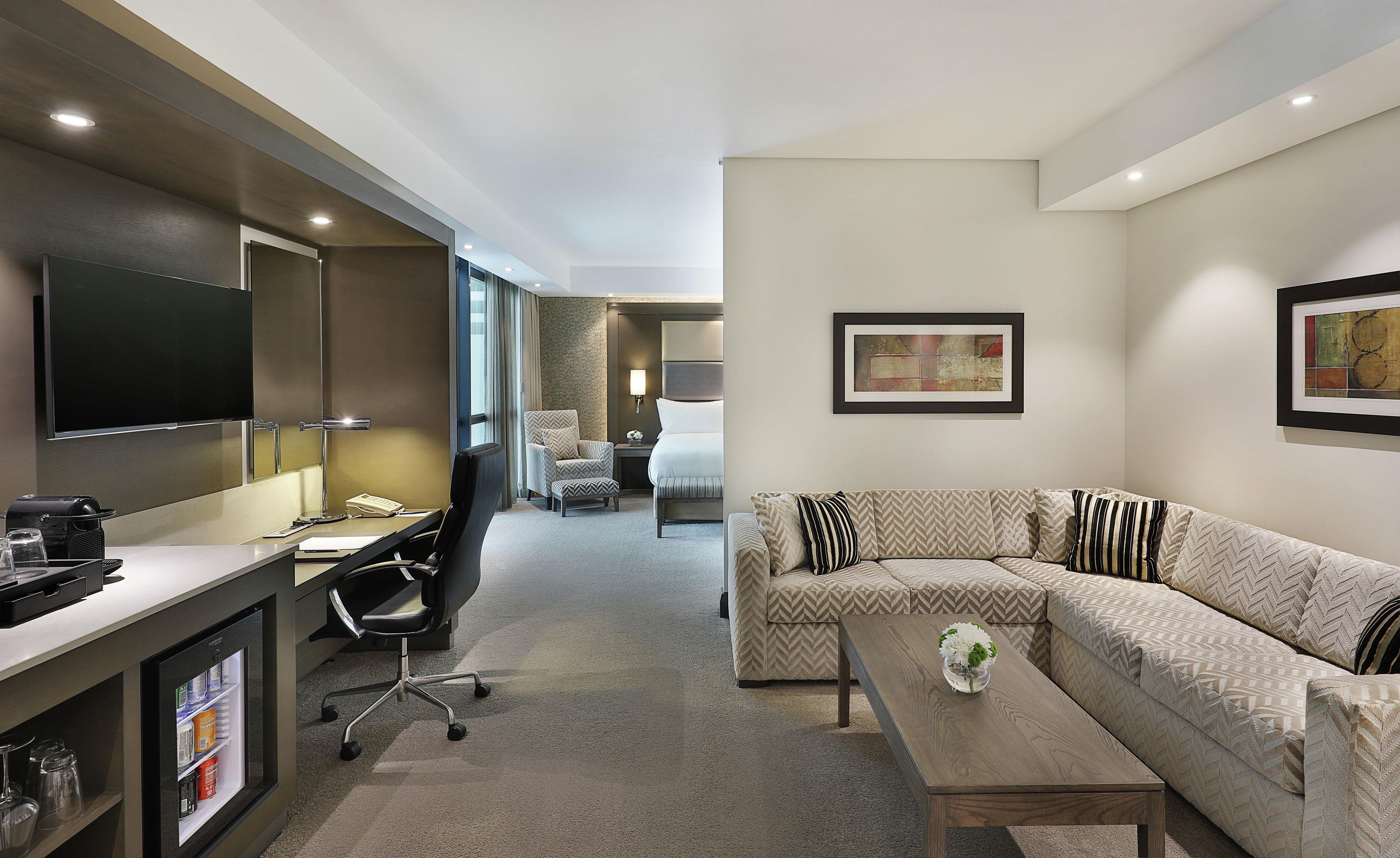 A hotel room with a flat-screen TV, a desk with a lamp, a sofa, and a coffee table.