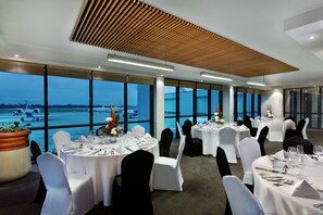 A conference room with round tables, white tablecloths, and black chairs. Large windows offer a view of an airport. - Legend Hotel Lagos Airport, Curio Collection by Hilton (Lagos)