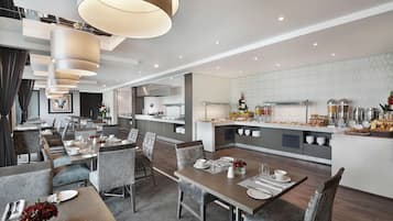 Et moderne hotelspiseområde med flere borde, stole og et centralt køkkenområde.