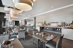 A modern hotel dining area with multiple tables, chairs, and a central kitchen area. - Legend Hotel Lagos Airport, Curio Collection by Hilton (Lagos)